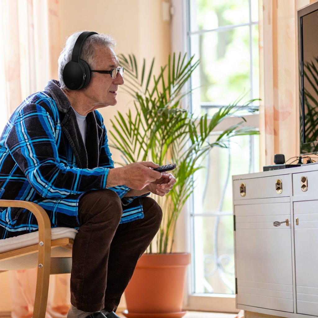 Senior man wearing wireless TV headphones while using a remote to watch television, enjoying clear and personalized sound at home